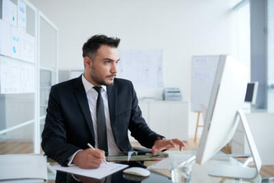 Professional IT staff writing and typing on a computer.